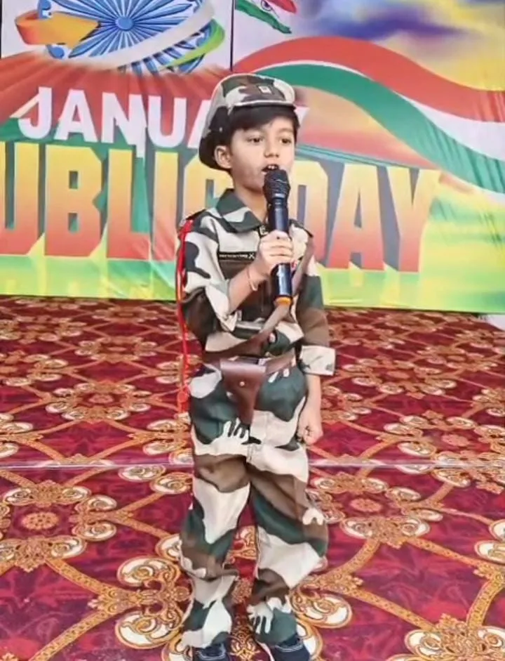Young child dressed in army uniform holding a microphone and speaking on stage with Republic Day backdrop during school celebration event.