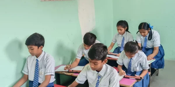 Students seated in classroom writing in notebooks while focusing on their work and participating in an academic learning session.