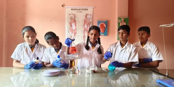 Students in lab coats using test tubes and measuring liquids during a science experiment in the classroom at Gnyan Oak School.