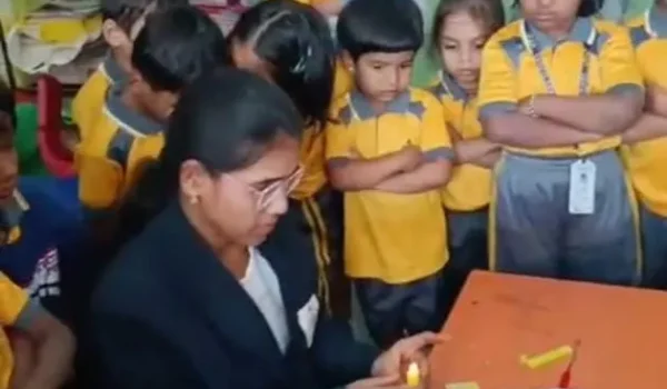 Teacher demonstrating activity with small objects on table while students stand around watching and learning through hands-on practice.