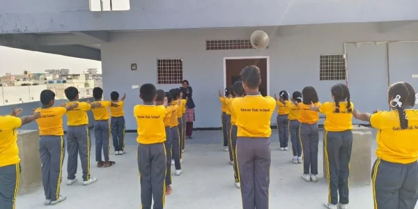 Students in yellow uniforms standing in rows on terrace ground performing a coordinated drill with discipline and teamwork.