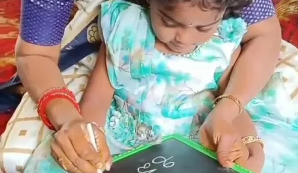 Adult guiding young child holding chalk and writing on a small slate board at Gnyan Oak School during an early learning activity session.