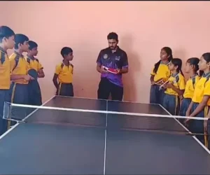 Students standing around a table tennis table while coach holds paddle and explains the game during an engaging sports activity session.