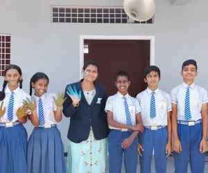 Teacher standing with students in uniform smiling together in front of the school building, showing a friendly and supportive learning environment.